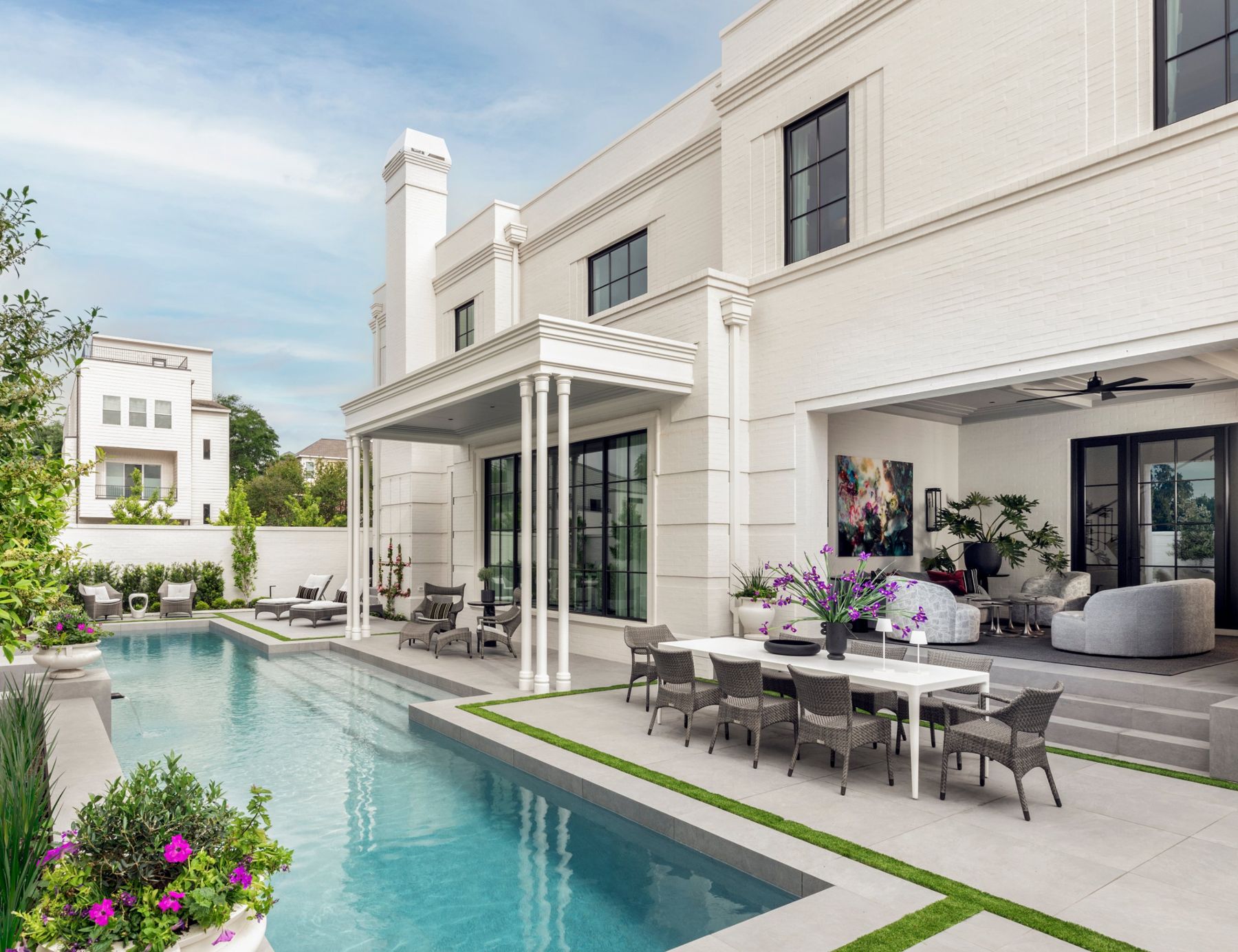 White brick home with a columned porch, covered outdoor living room and a long pool